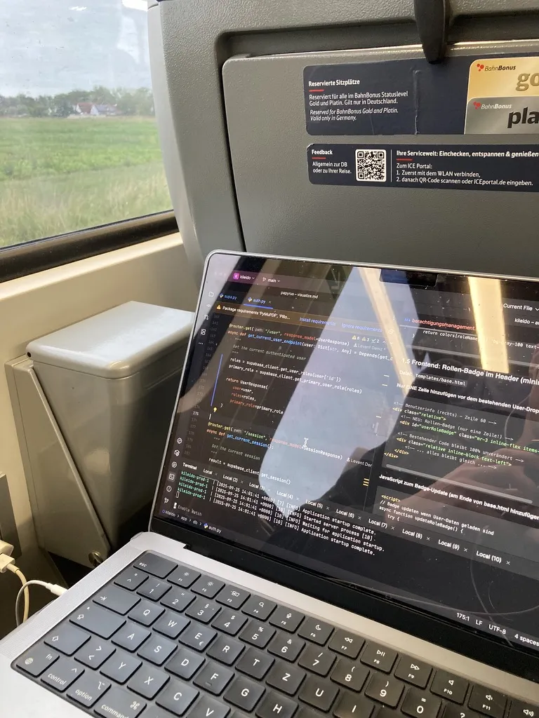 Laptop mit Code auf dem Klapptisch eines ICE, draußen zieht die Landschaft vorbei